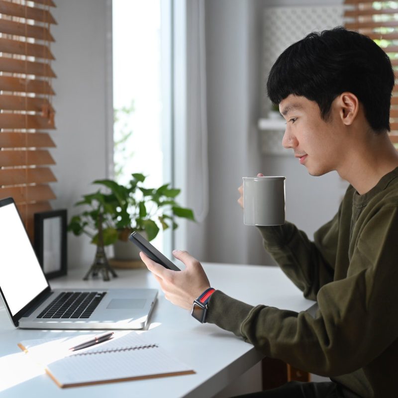 side-view-of-young-businessman-drinking-coffee-an-checking-social-media-on-mobile-phone-.jpg